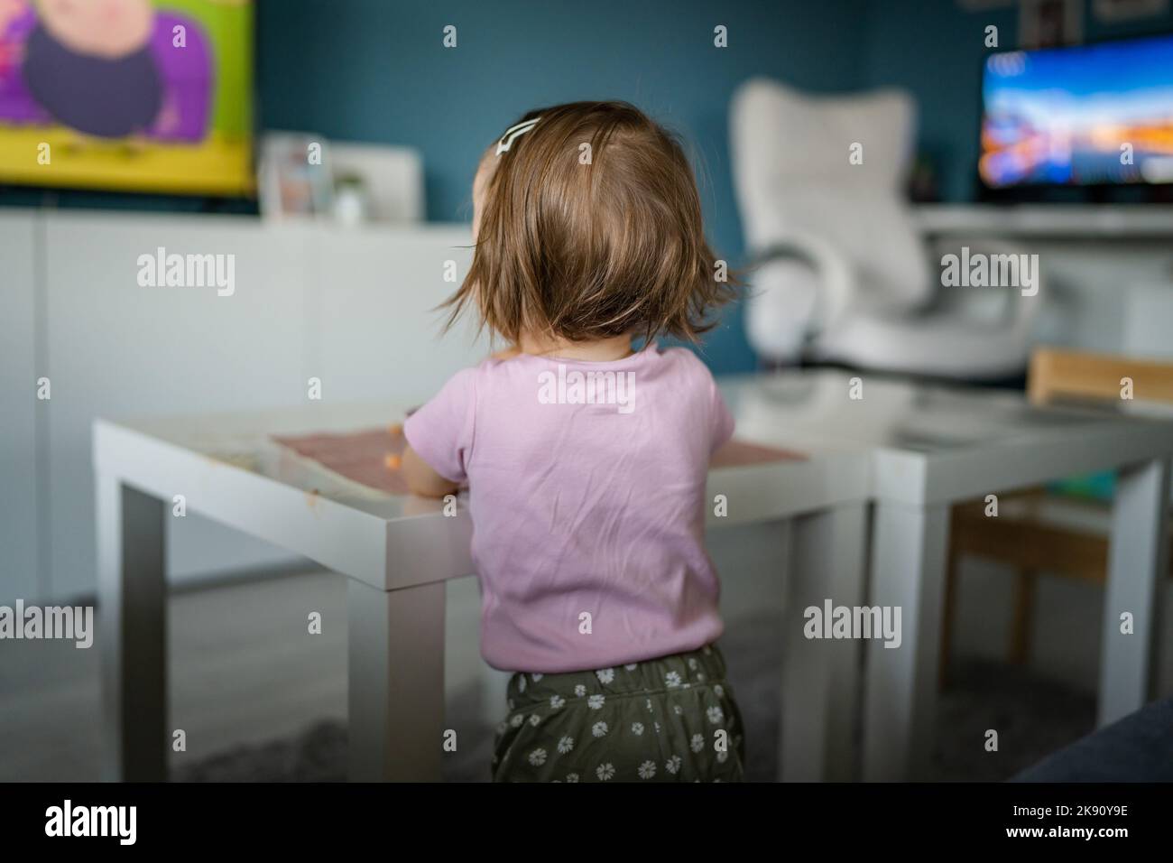 Vista posteriore di una ragazza bambino caucasica sconosciuta in piedi a casa guardando la tv mentre mangiando l'infanzia spazio copia crescere sviluppo di svago co Foto Stock