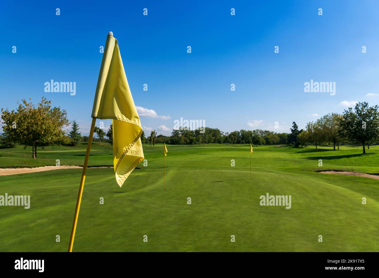 Pole con bandiera gialla per la posizione di pin sul campo erboso verde per il gioco di golf nel parco sotto il cielo blu Foto Stock