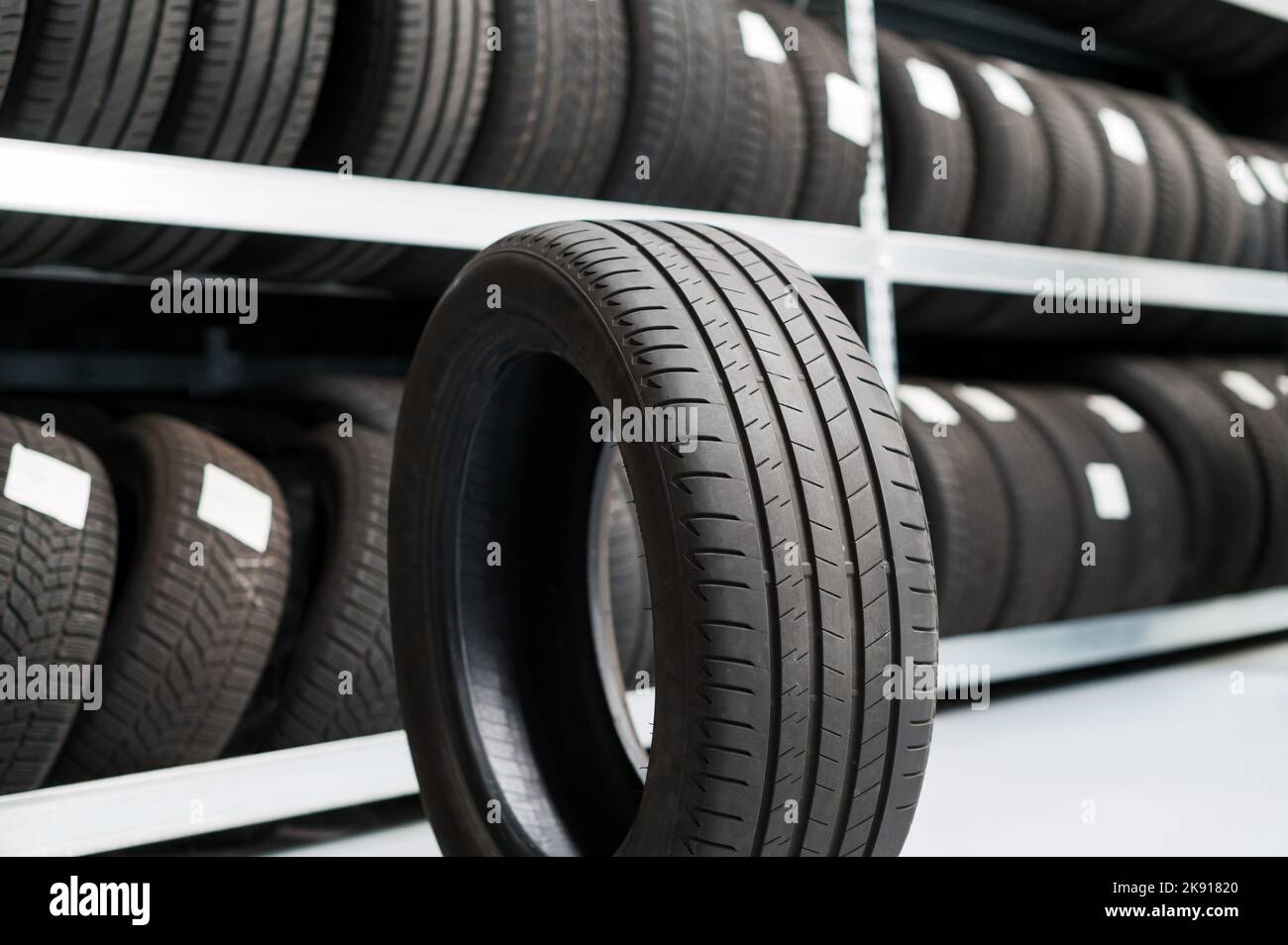 Nuovo pneumatico di auto nero fresco sul pavimento vicino al banco stack con pneumatici nel negozio moderno Foto Stock
