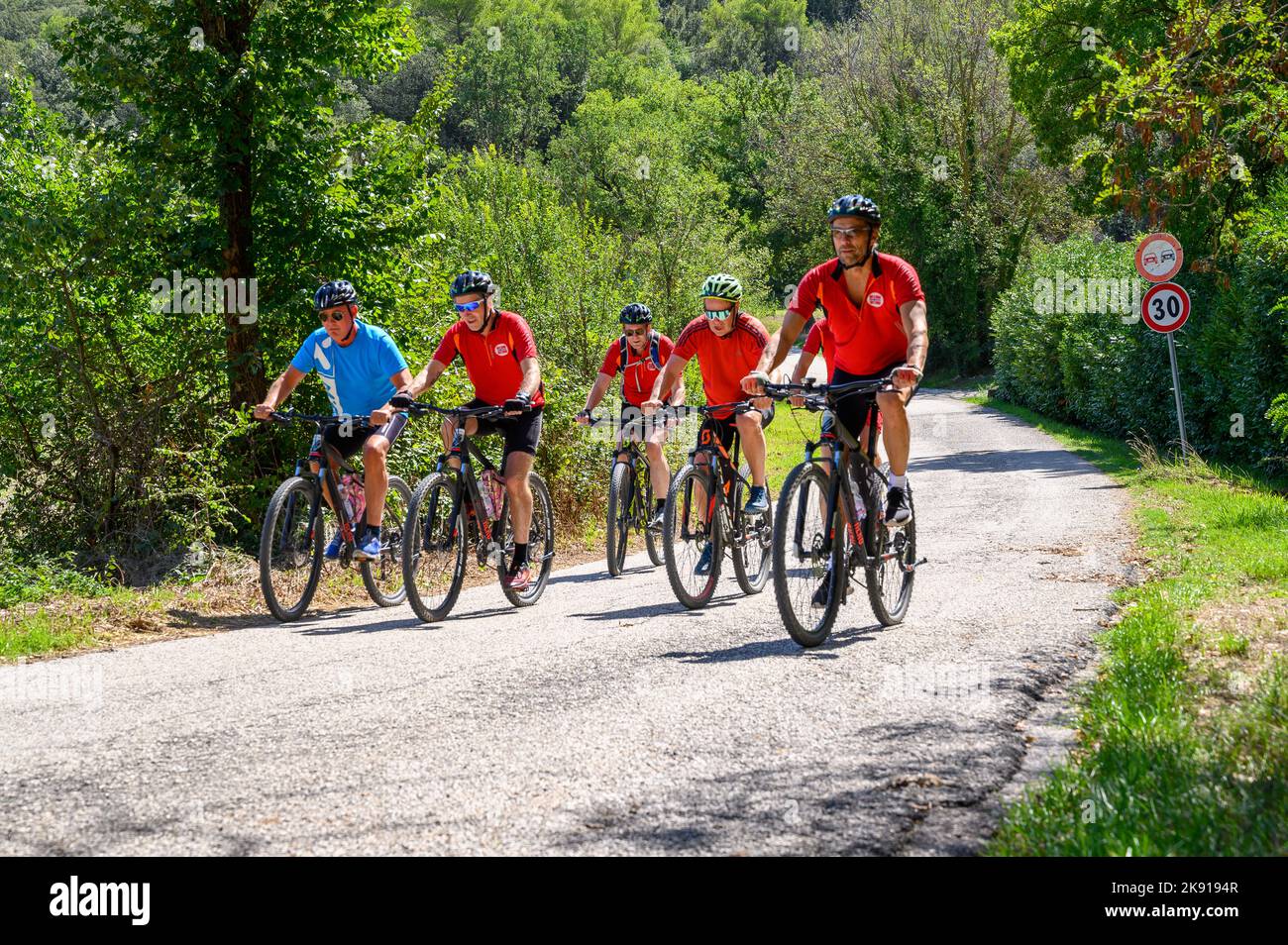 Un gruppo di ciclisti norvegesi di mezza età in bicicletta noleggiata percorrendo una strada collinare nel paesaggio umbro vicino a Spoleto, Umbria, Italia. Foto Stock