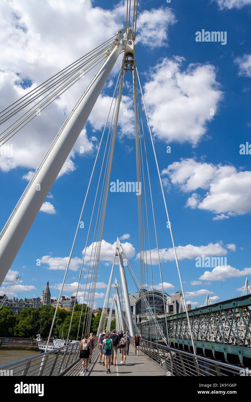 Golden Jubilee Bridge accanto al ponte ferroviario di Hungerford sul Tamigi, Londra, Regno Unito. Persone che camminano attraverso il ponte pedonale con i cavi Foto Stock