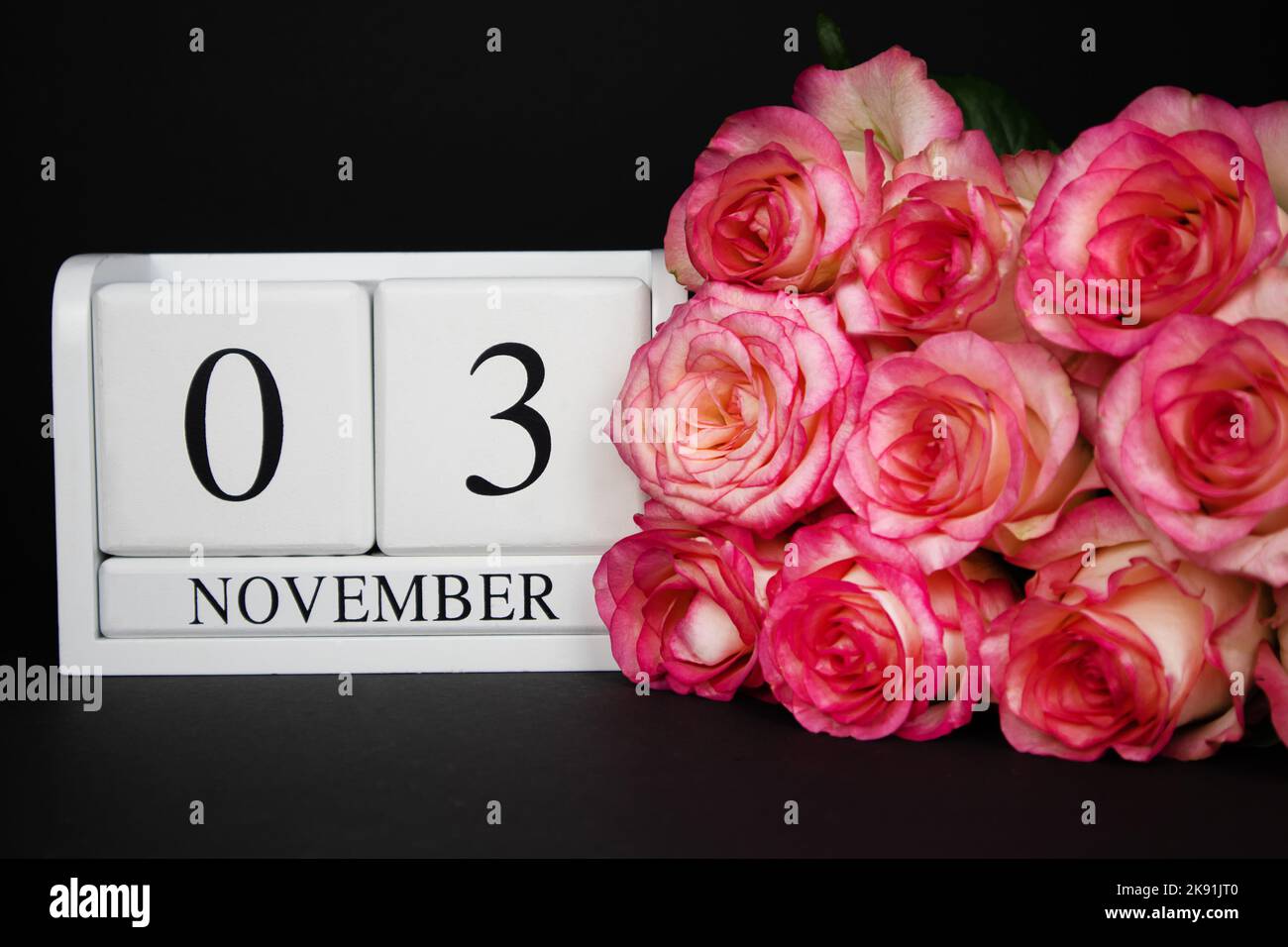 Novembre 3 calendario in legno, bianco su sfondo nero, rosa rose giacciono nelle vicinanze. Foto Stock