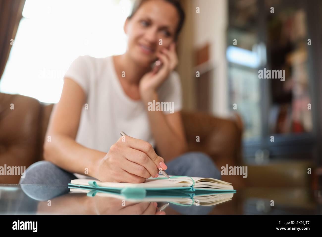 Donna che parla al telefono e scrive qualcosa sul blocco note Foto Stock