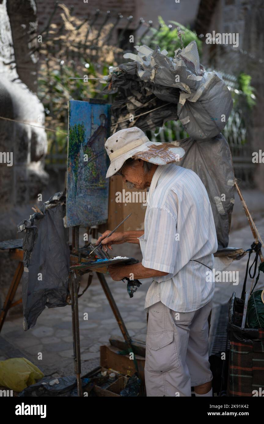 Un gentleman asiatico anziano dipinge un quadro sulla strada in una giornata di sole estate Foto Stock
