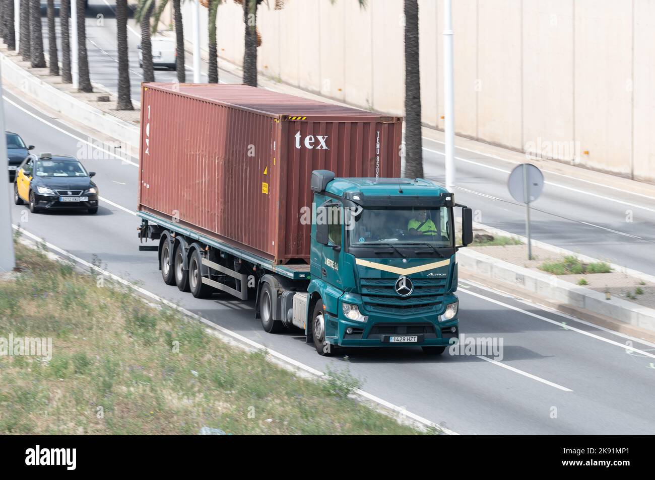 Camion Mercedes Actros verde che carica un rimorchio container rosso lungo la Ronda Litoral di Barcellona Foto Stock