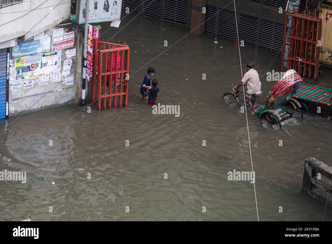 I proprietari di risciò lottano per attraversare una strada bagnata a seguito di forti piogge causando molta sofferenza per pedoni e pendolari. Cyclone Sitrang colpisce il Bangladesh strappando comunicazioni e collegamenti elettrici, inondando le strade portando le attività a uno stand fermo. Foto Stock