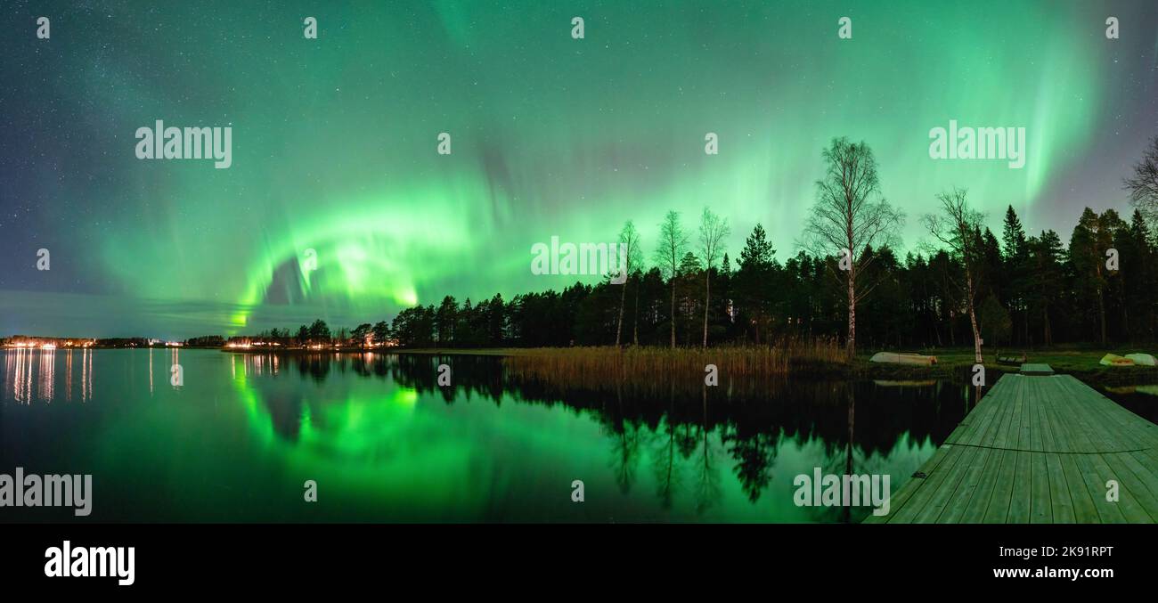 Spettacolare panorama notturno, luci verdi forti di aurora danzante sulla foresta settentrionale, riflesso nel lago, piccola barca, ponte. Lago Stocksjo Foto Stock