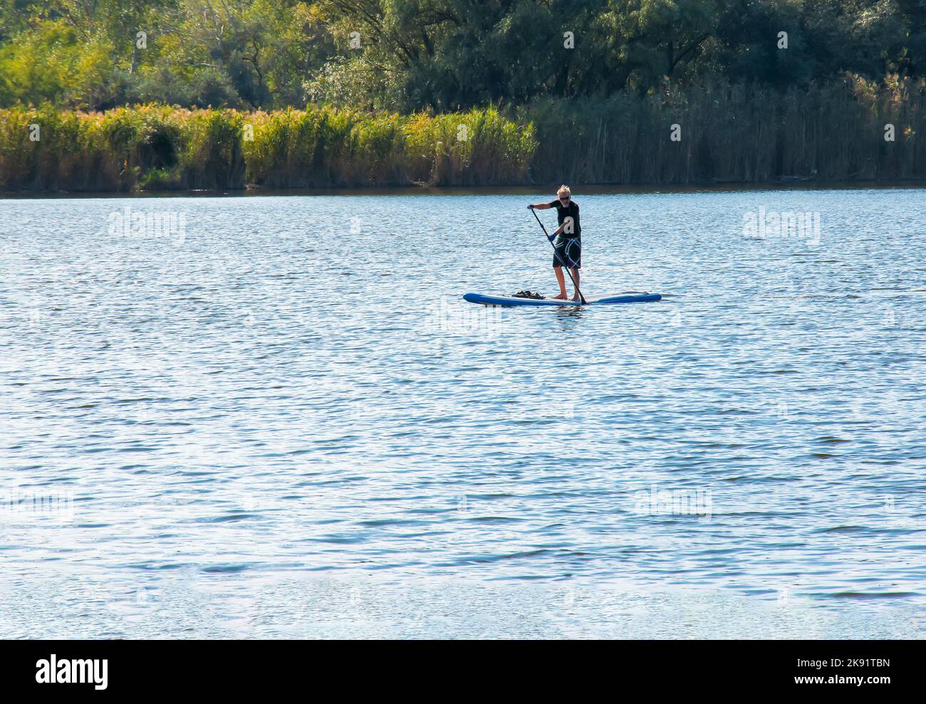 Dnipro, Ucraina - 09.08.2022: Un uomo sportivo di anni avanzati cavalca uno zapboard sul fiume. Set di foto. Attività acquatiche in città. Foto Stock