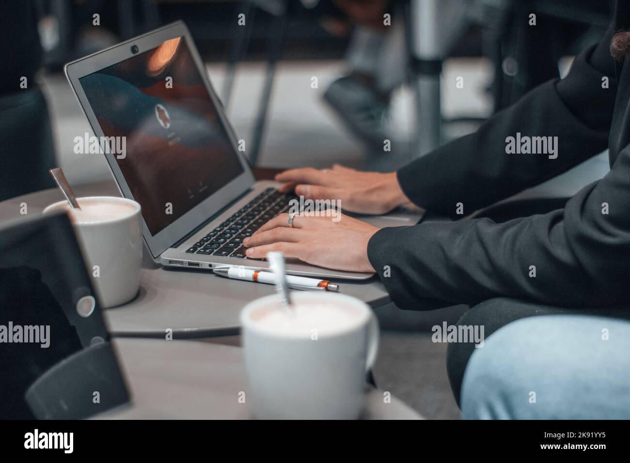 Una vista delle mani di una donna che digita su un notebook con una tazza di caffè sul suo tavolo Foto Stock