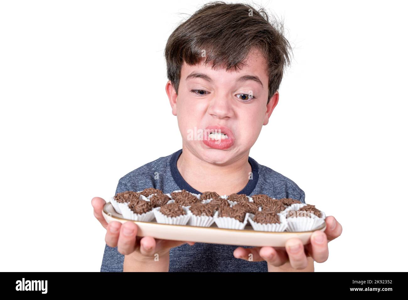 Brasiliano di 9 anni che tiene un vassoio con diverse palline fudge brasiliane e facendo un volto arrabbiato. Foto Stock