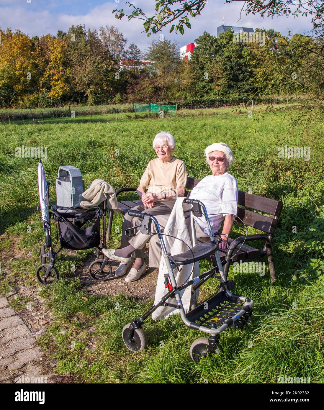 SCHWALBACH, GERMANIA - Oct 19, 2014: Due donne anziane godono il sole su una panca e vi hanno ottenuto con un telaio a piedi, un aiuto medico per il walki Foto Stock