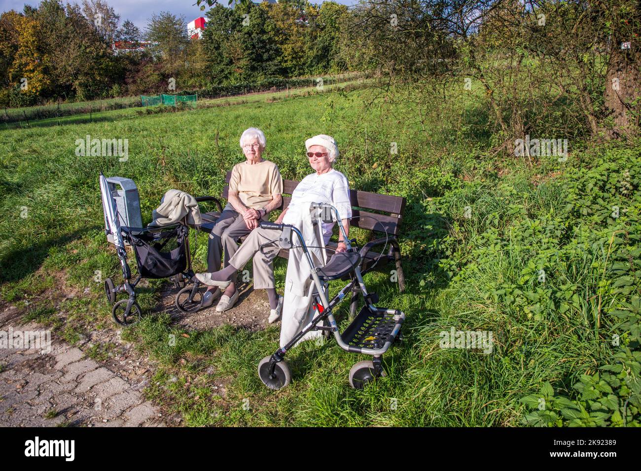 SCHWALBACH, GERMANIA - Oct 19, 2014: Due donne anziane godono il sole su una panca e vi hanno ottenuto con un telaio a piedi, un aiuto medico per il walki Foto Stock