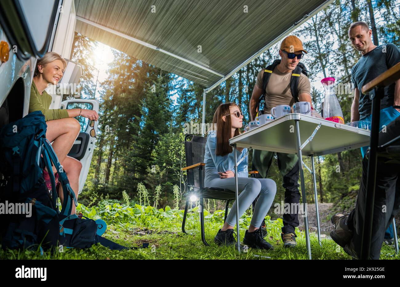 Famiglia caucasica felice godendo il tempo del tè fuori del loro RV durante la sosta nel Woods. Giornata di sole tra la natura. Tema di viaggio per camper. Foto Stock