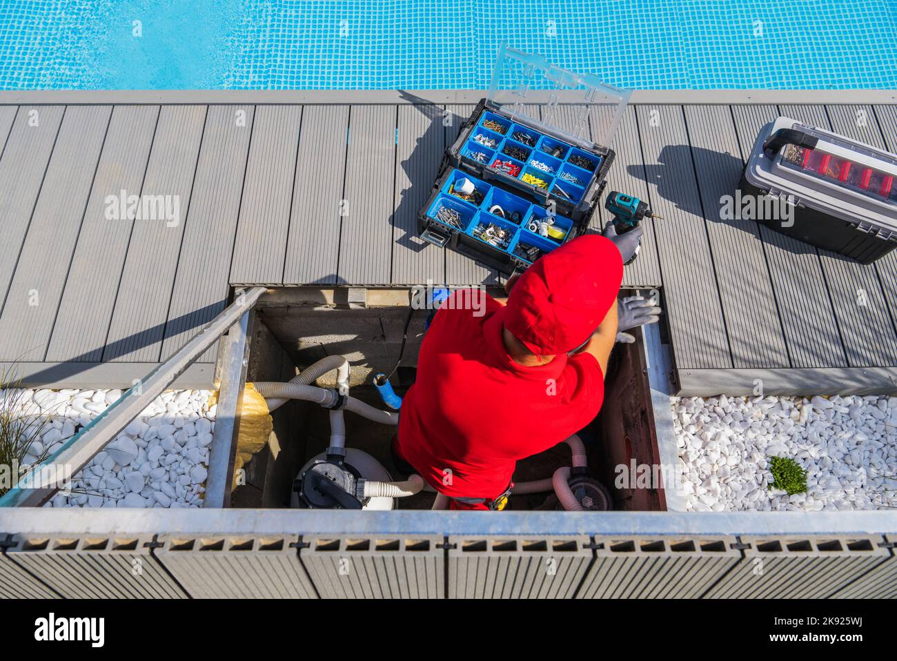Tecnico professionista in uniforme rossa che esegue le normali procedure di manutenzione del pool. Aprire Toolbox con strumenti e componenti diversi davanti a Hi Foto Stock