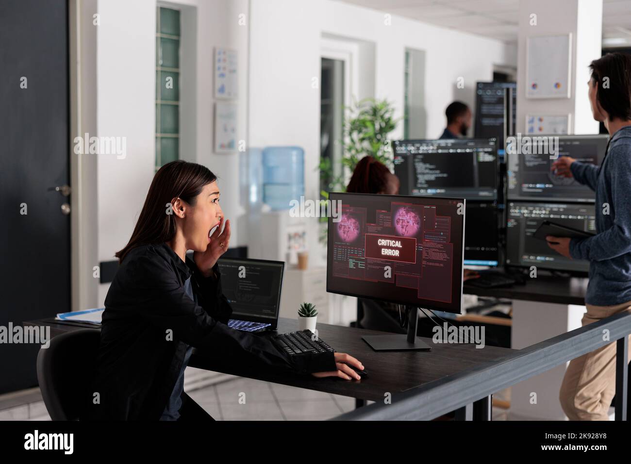 Programmatore IT asiatico che legge gli errori critici sul display del computer in un'agenzia IT per i big data, essendo violato. Lavorare con il codice di intelligenza artificiale e il database dei server per fermare l'hacking del programma. Foto Stock