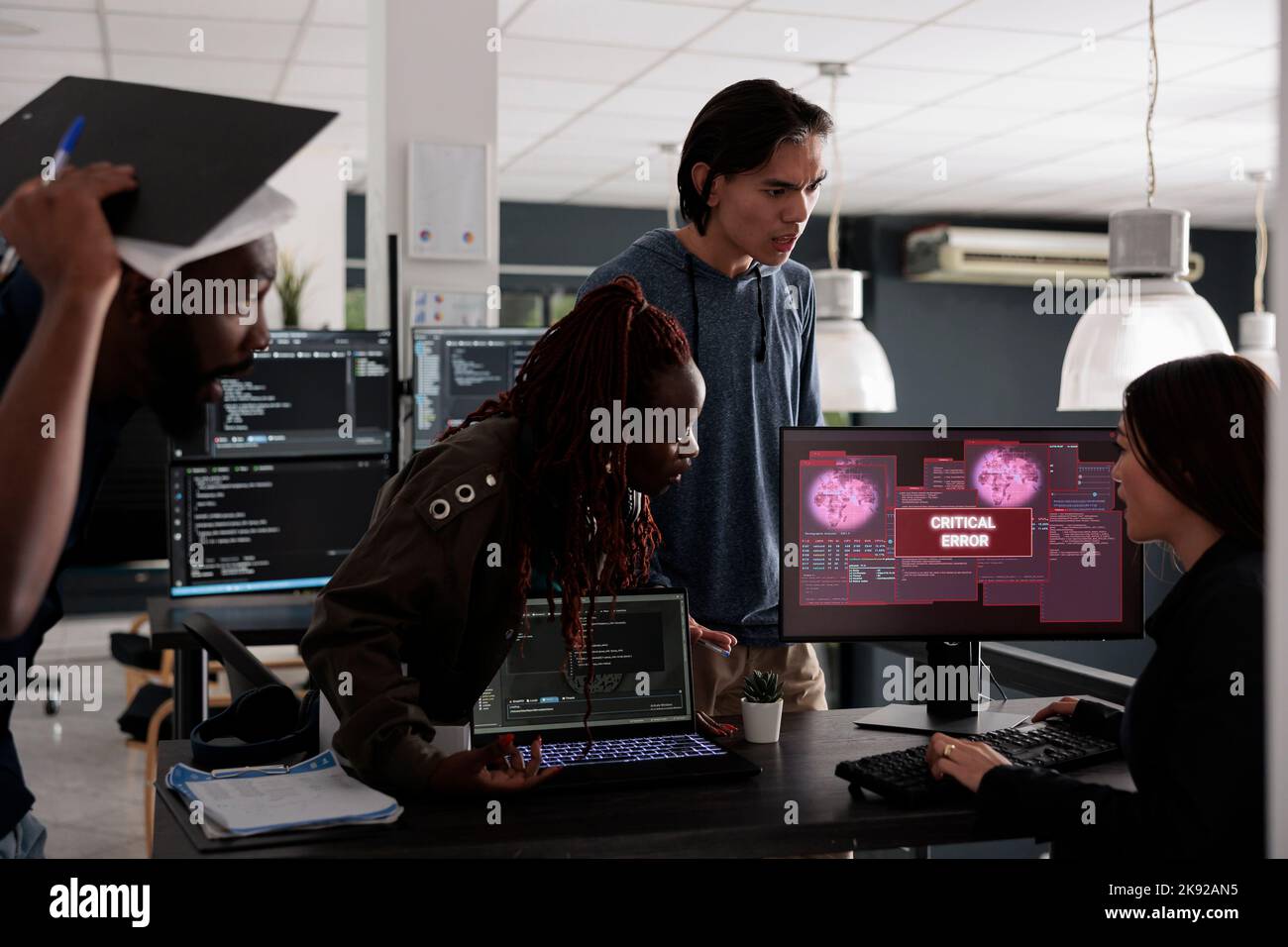 Programmatori multietnici che hanno un avviso di violazione della sicurezza sullo schermo del computer, cercando di risolvere l'hacking e l'errore critico. Ingegneri che utilizzano la finestra del terminale e che hanno violato il sistema crash. Foto Stock