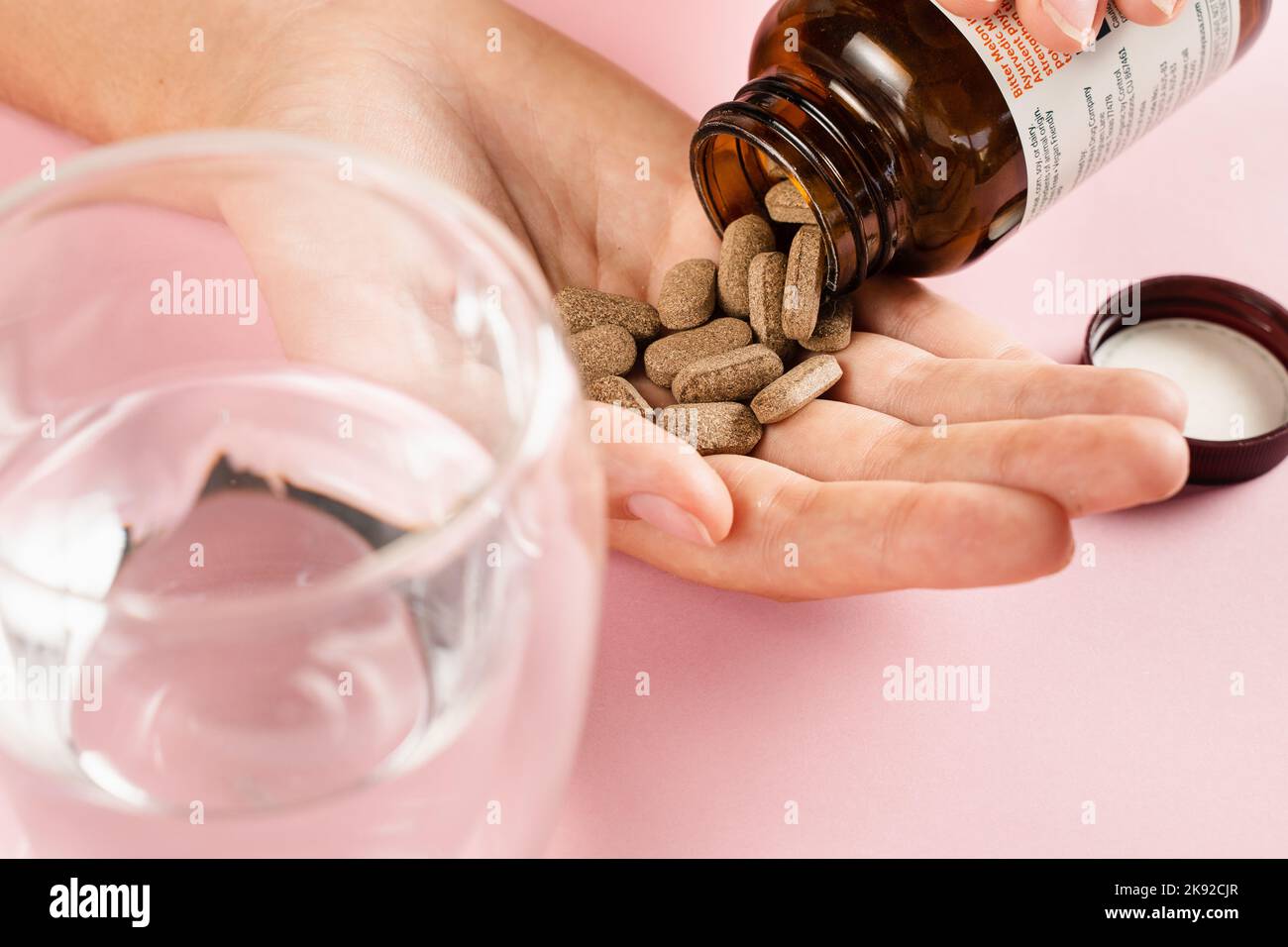 Bottiglia di pillole di perdita di peso e bicchiere d'acqua su sfondo rosa. Concetto di nutrizione adeguato. Pillole di tenuta per la dieta in mano e pronto per bere acqua. Foto Stock