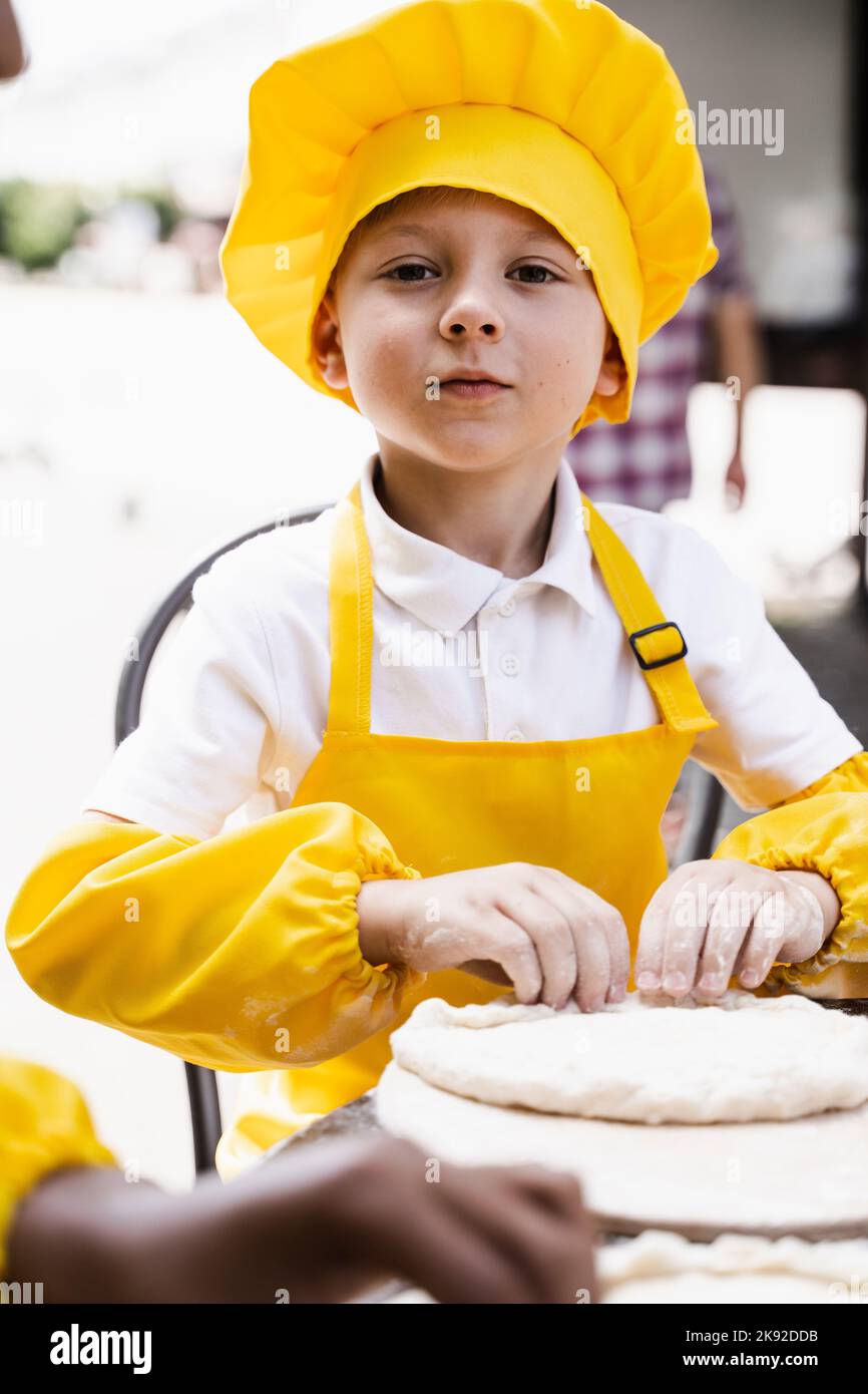 Bel cuoco bambino in giallo chef cappello e grembiule giallo uniforme  cottura e tenere rullo pasta all'aperto Foto stock - Alamy
