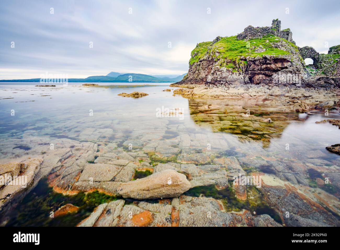 Vicino alle acque tranquille con la bassa marea, a metà estate, resti di un antico, storico castello scozzese, vista, superficie liscia del Loch e molte boul Foto Stock