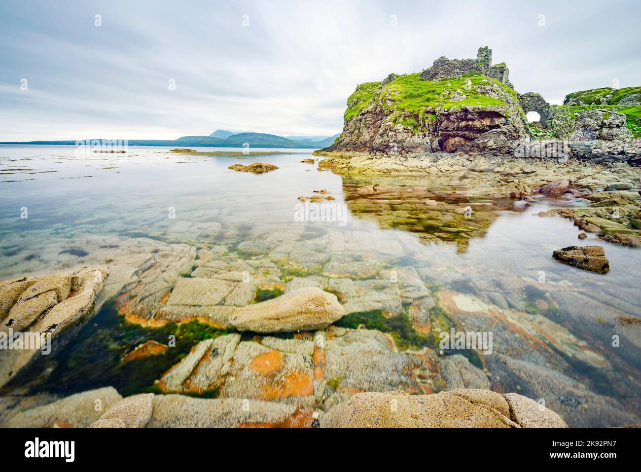 Vicino alle acque tranquille con la bassa marea, a metà estate, resti di un antico, storico castello scozzese, vista, superficie liscia del Loch e molte boul Foto Stock