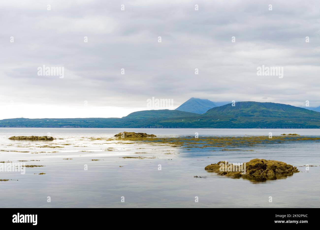 Il tranquillo, tranquillo mare estivo, tardo pomeriggio sul Loch, rocce che sporgono dalla superficie dell'acqua guardando verso le montagne lontane vicino Elgol, su t Foto Stock