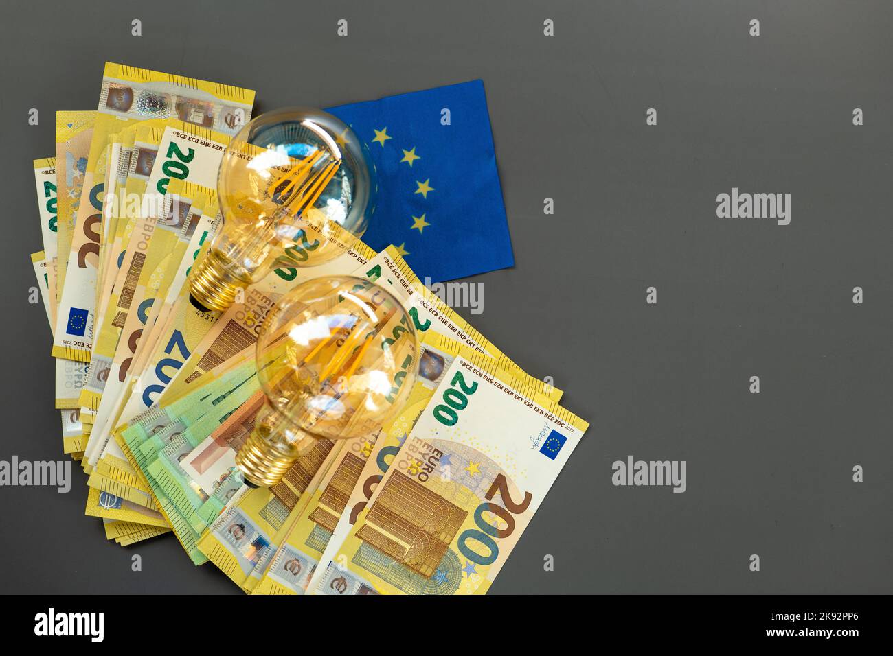 Lampadine e bollette in euro e la bandiera dell'UE su uno sfondo grigio scuro.Rising elettricità prices.Paying bollette in Europa. Foto Stock