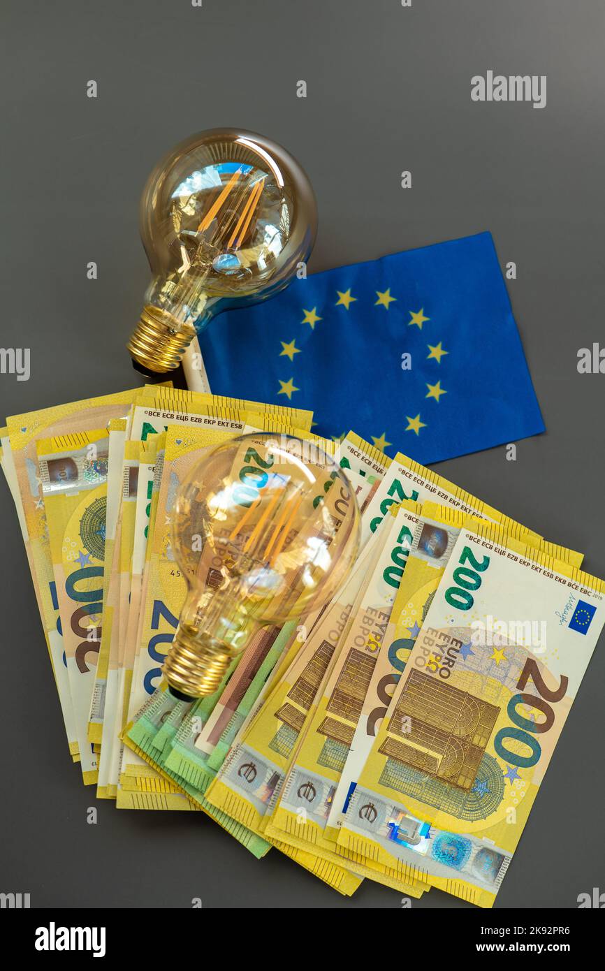 Lampadine, bollette in euro e bandiera dell'UE su sfondo grigio scuro. Aumento dei prezzi dell'elettricità. Foto Stock