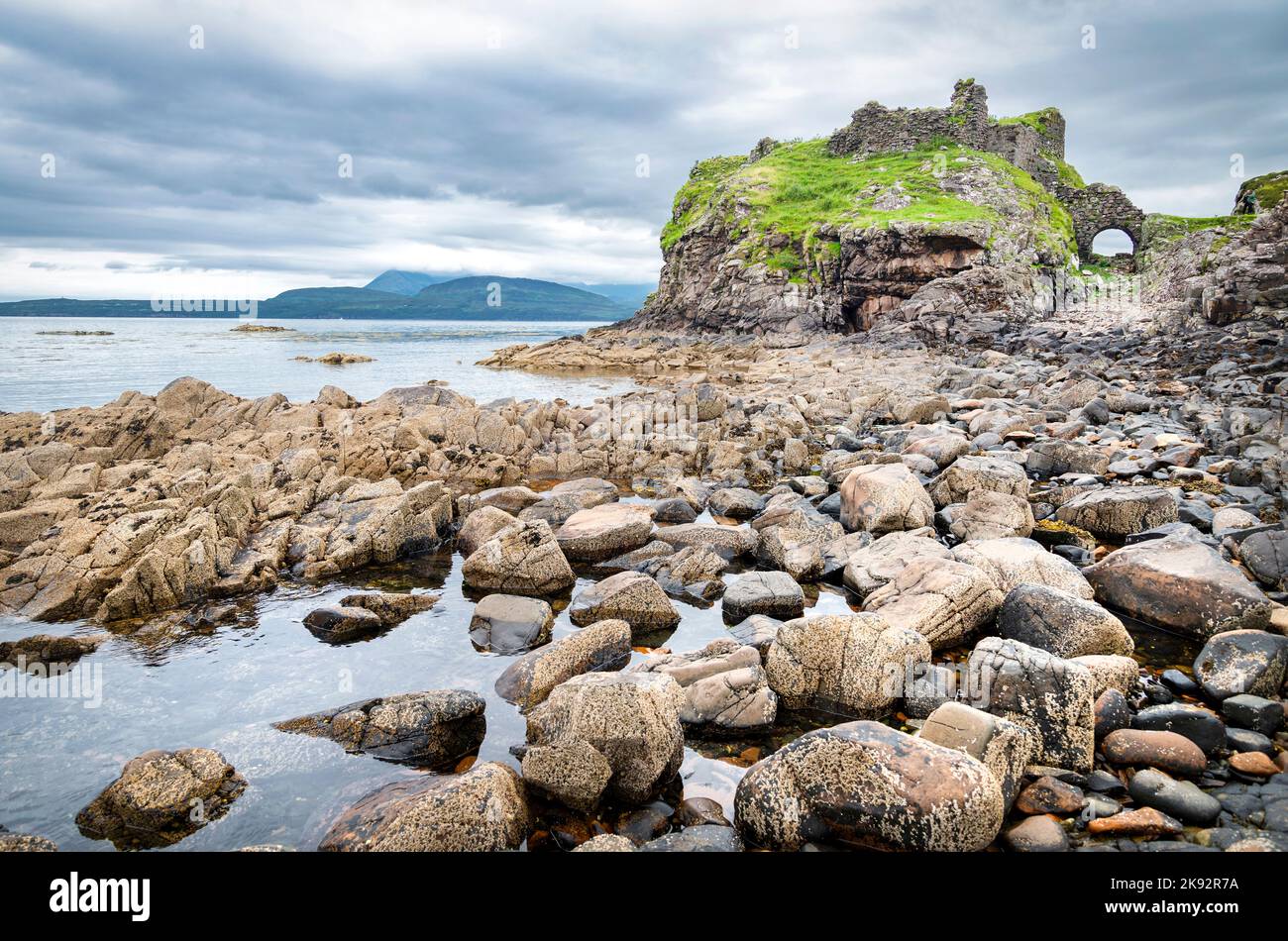 Vicino alle acque tranquille con la bassa marea, a metà estate, resti di un antico, storico castello scozzese, vista, superficie liscia del Loch e molte boul Foto Stock