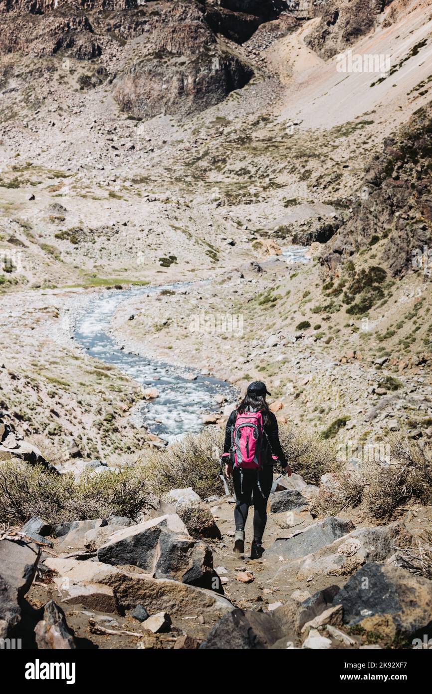 Vista posteriore di escursionismo femminile backpacker attraverso un sentiero roccioso accanto a un fiume di montagna. Scatto verticale Foto Stock