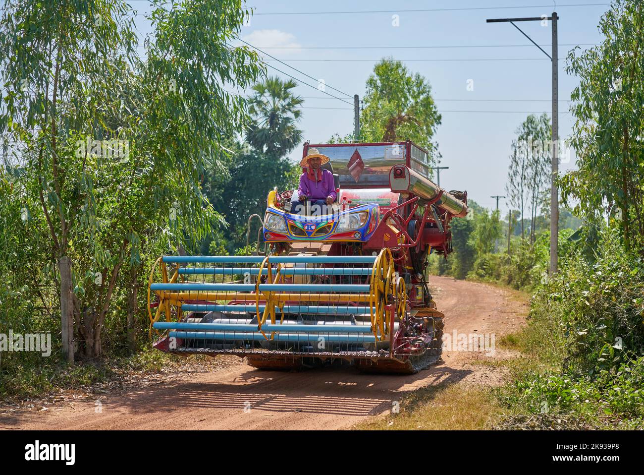 Un uomo siede su una macchina per la raccolta del riso su una piccola strada rurale in Thailandia. Foto Stock