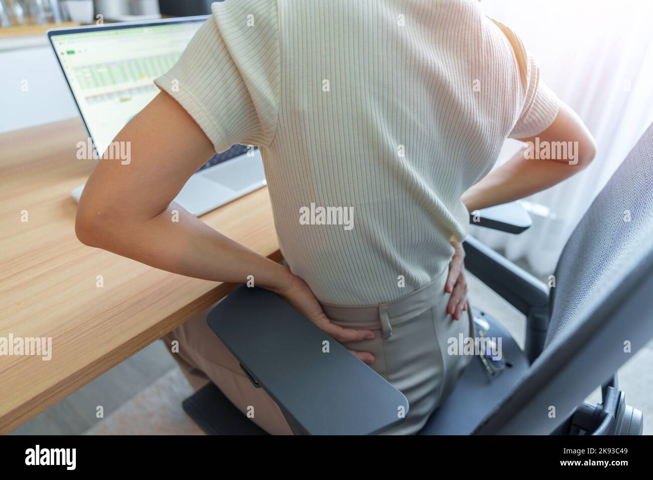 Donna con dolore alla schiena durante il lavoro a lungo sul posto di lavoro. A causa di Piriformis, schiena bassa, mal di vita, lombaggine, rene, Reumatismi e comppre spinale Foto Stock