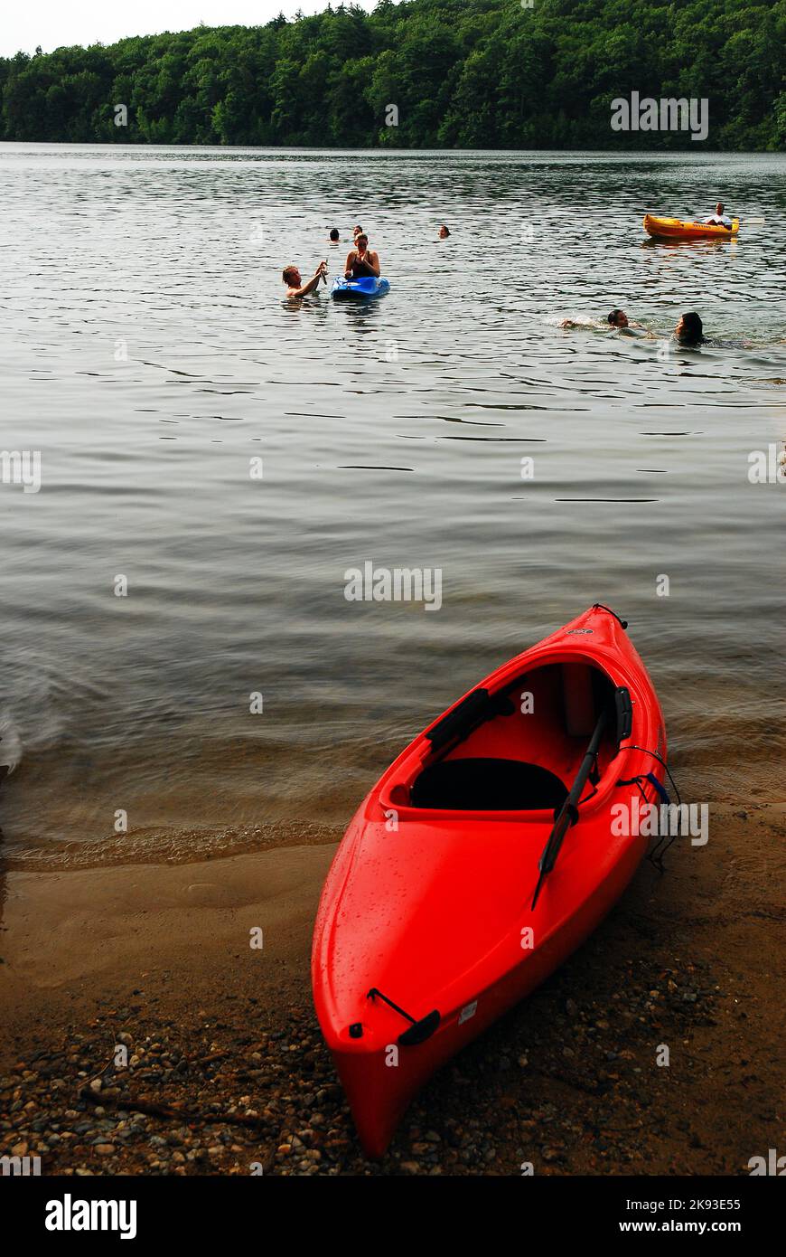 Un kayak attende un cavaliere sulla riva del lago, mentre altri vanno a nuotare nello stagno in una giornata di vacanze estive Foto Stock