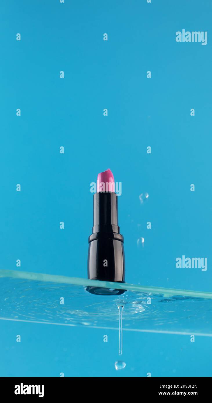 Rossetto rosa su una mensola di vetro su uno sfondo blu con goccia d'acqua. Foto Stock