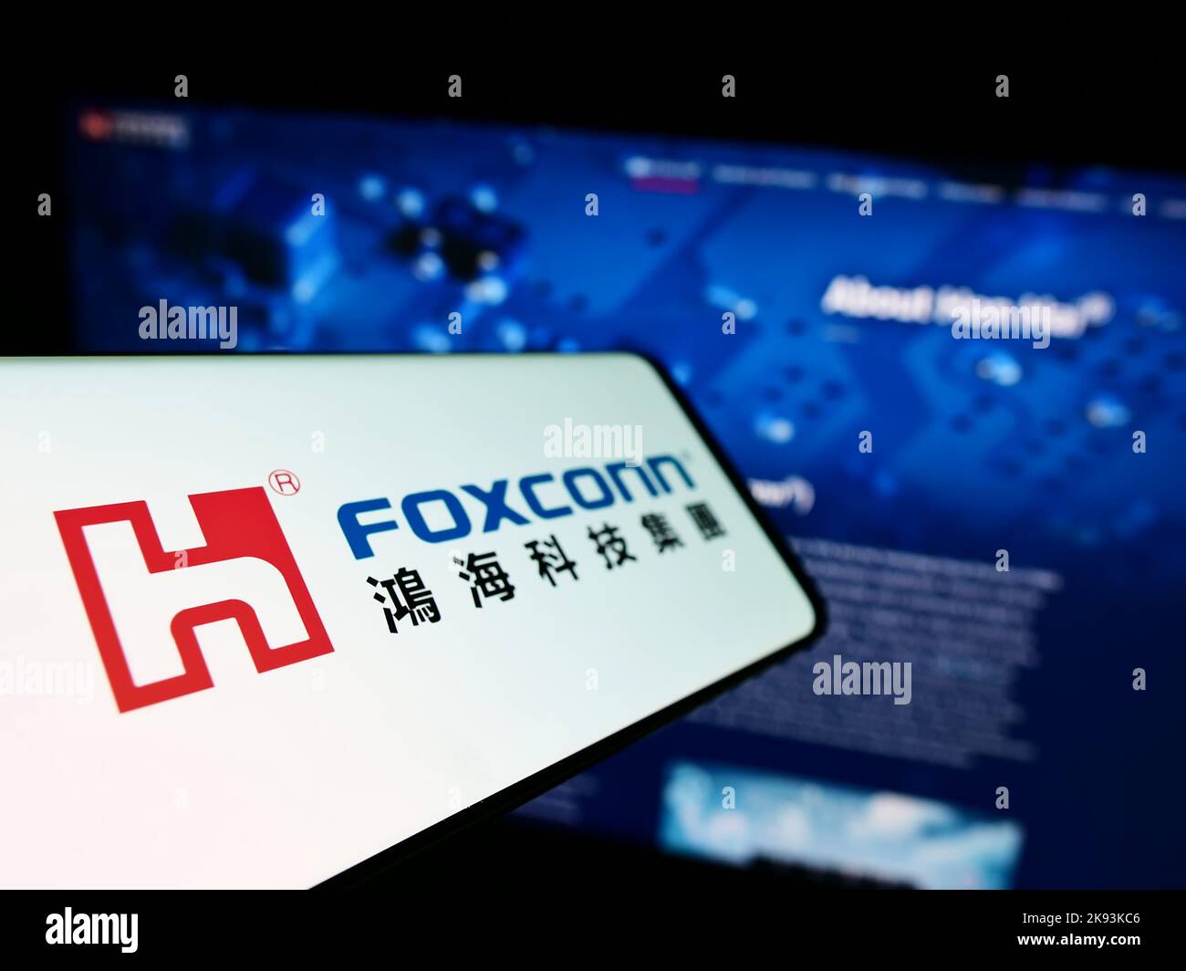Smartphone con logo di Hon Hai Precision Industry Co. Ltd. (Foxconn) sullo schermo di fronte al sito Web aziendale. Messa a fuoco a sinistra del display del telefono. Foto Stock