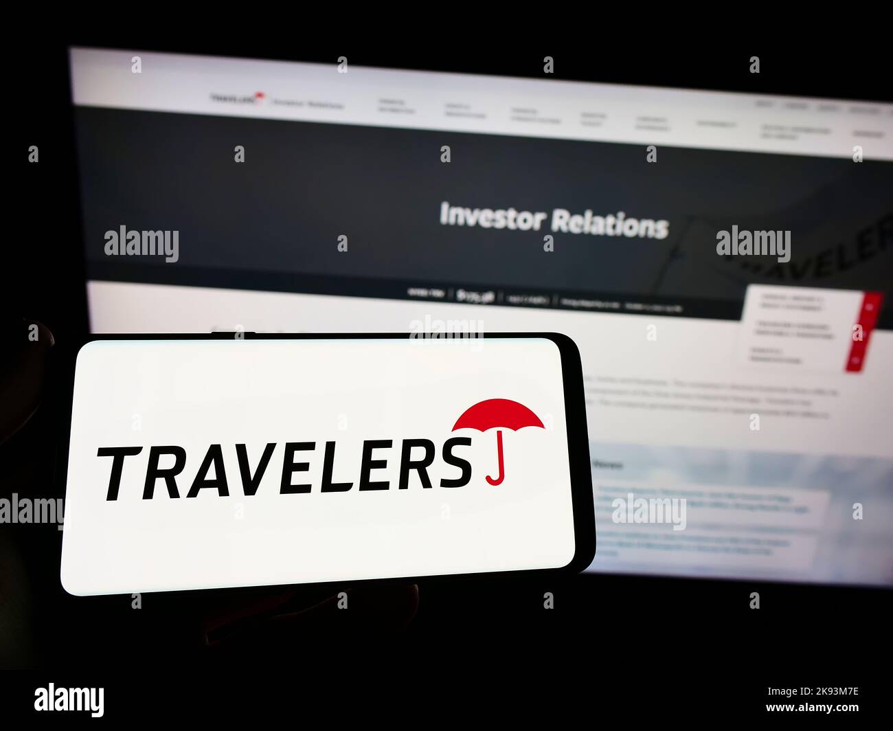 Persona che detiene il telefono cellulare con il logo della compagnia di assicurazione statunitense The Travellers Companies Inc. Sullo schermo di fronte alla pagina web. Messa a fuoco sul display del telefono. Foto Stock