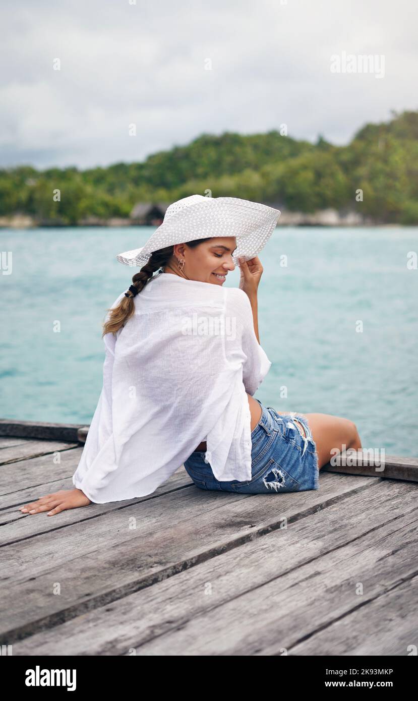 Il mio posto preferito per le vacanze è vicino all'oceano, una giovane donna che si siede sul bordo di una passerella e che si gode una brezza durante le vacanze. Foto Stock