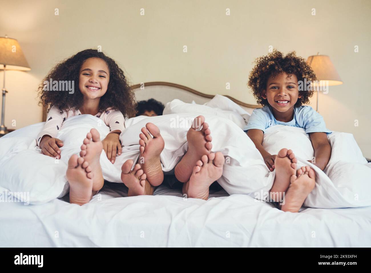 Svegliarsi come una famiglia felice. Ritratto di due adorabili bambini che si rilassano a letto con i genitori a casa. Foto Stock