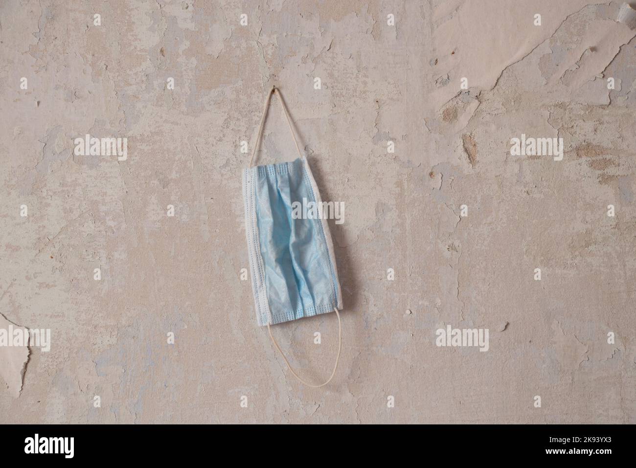 maschera medica appesa su un vecchio muro bianco a casa, quarantena Foto Stock