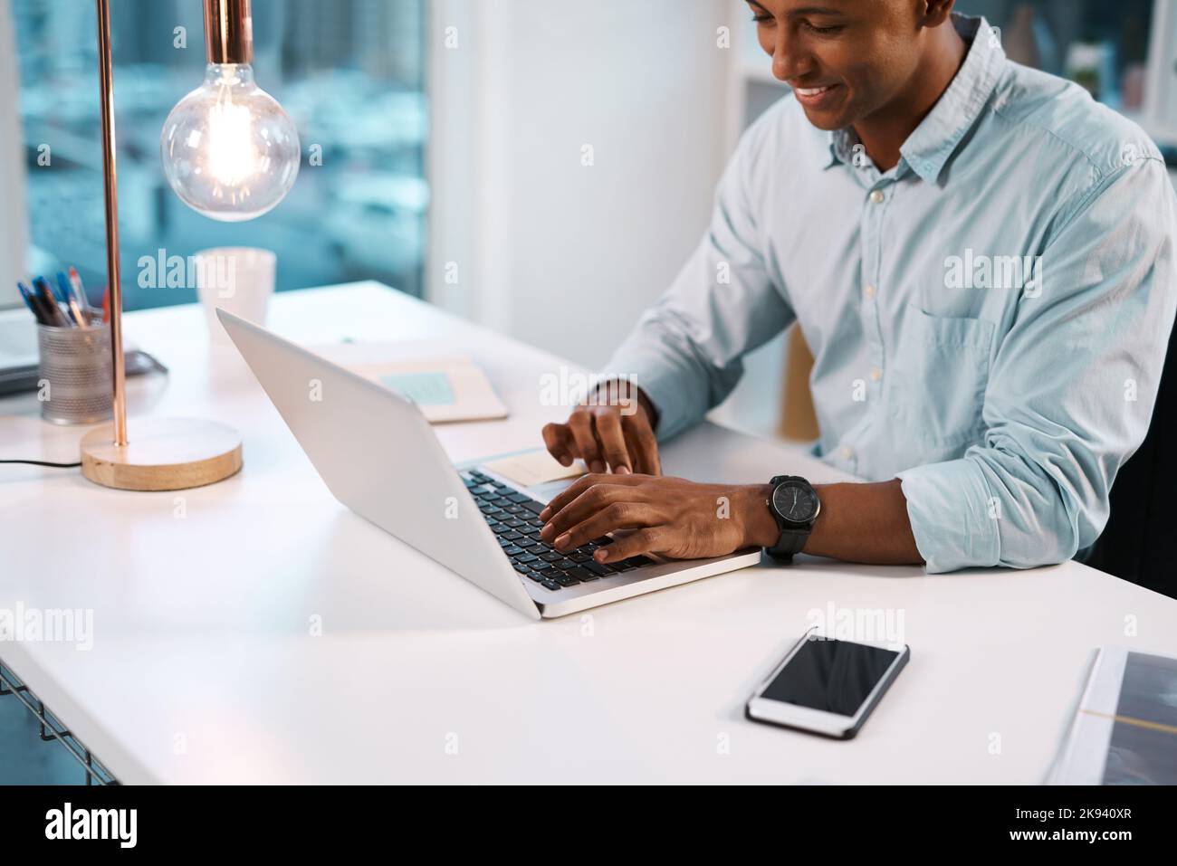 Lavora sempre con un sorriso sul viso. Un bel giovane uomo d'affari che lavora sul suo computer portatile durante un turno di tarda notte al lavoro. Foto Stock