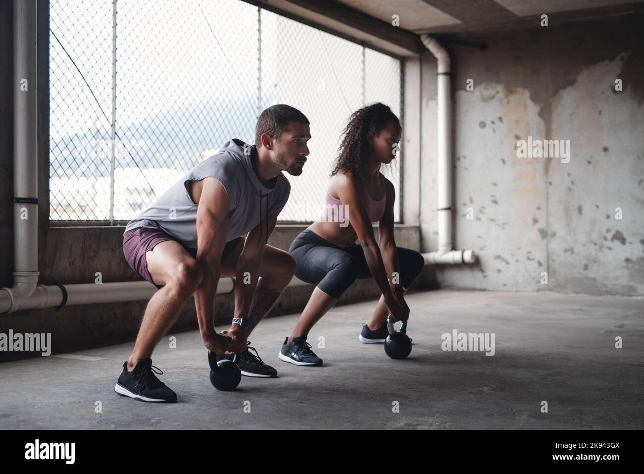 Sollevando ogni spiriti altri attraverso ogni workout. Scatto integrale di una giovane coppia sportiva che si allena con le campane all'interno di un parcheggio sotterraneo Foto Stock