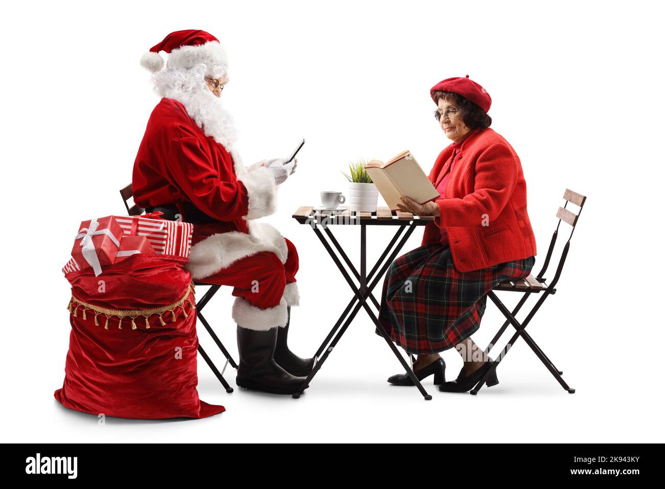 Babbo Natale con smartphone e una donna anziana seduta a un tavolo e libro di lettura isolato su sfondo bianco Foto Stock