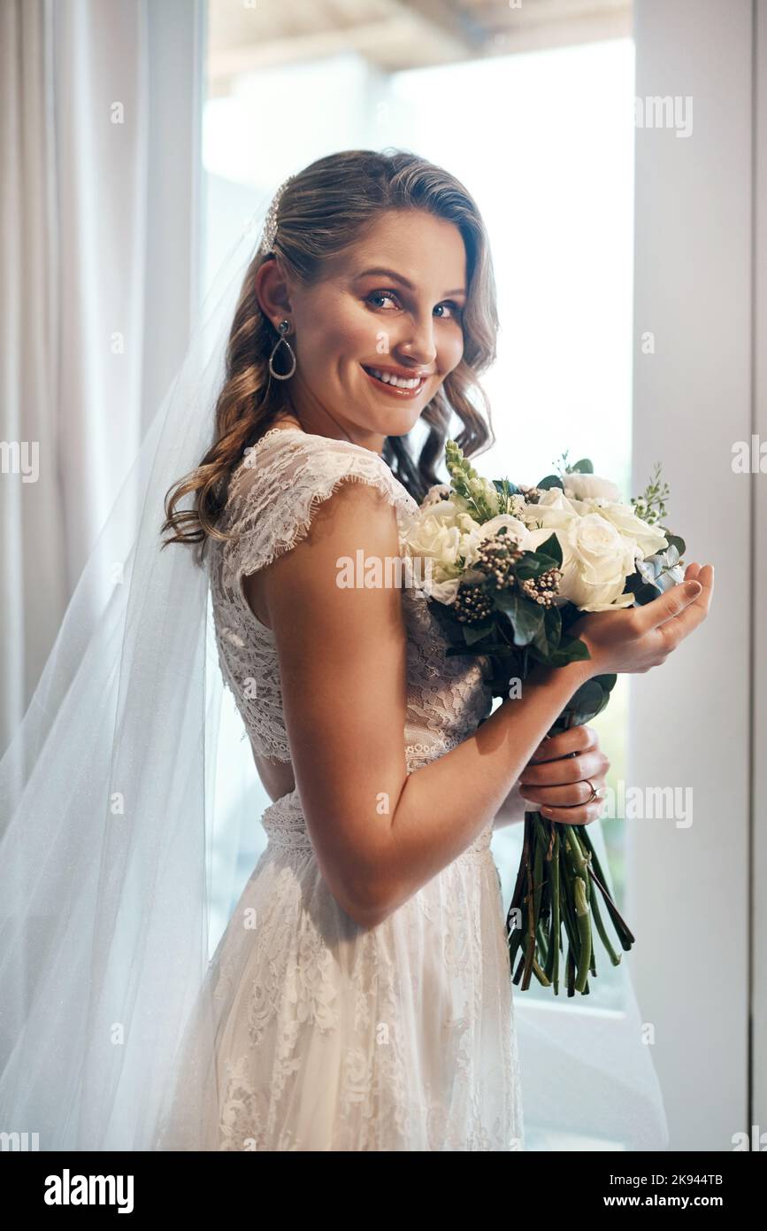 E così inizia l'avventura. Ritratto corto di una giovane sposa attraente in piedi da sola nello spogliatoio e tenendo il suo bouquet di fiori. Foto Stock