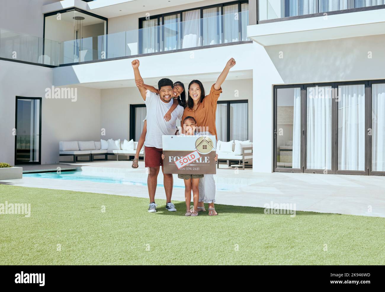 Famiglia felice, tavola venduta e nuova casa insieme celebrare all'aperto sul prato. Madre eccitata, sorriso padre e braccia bambini in aria felicità Foto Stock