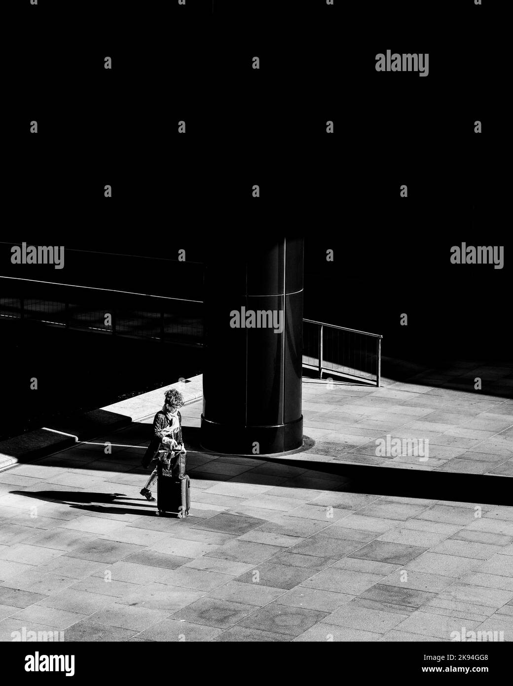 Una foto in scala di grigi di una donna anziana che cammina attraverso una piazza nel quartiere finanziario Foto Stock