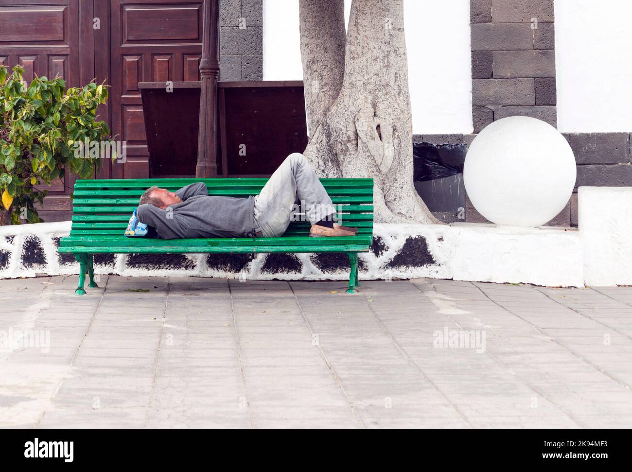Arrecife, Spagna - 3 aprile 2012: L'uomo tiene una siesta su una panchina ad Arrecife, Spagna. Siesta è il tradizionale orario di riposo da mezzogiorno alle 3:00 in Spagna. Foto Stock