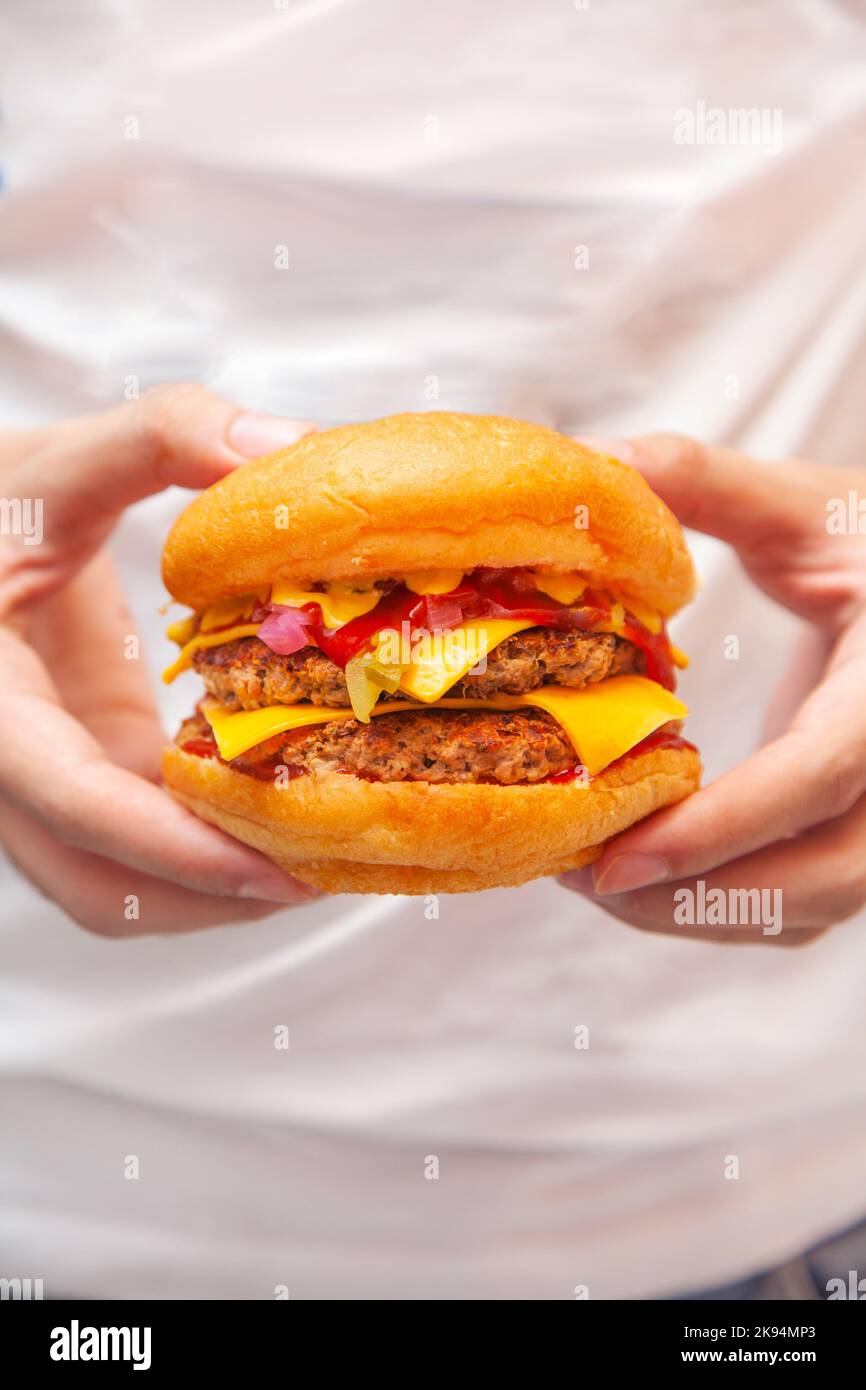 Hamburger con entrambe le mani indossando una camicia bianca e jeans. Foto Stock
