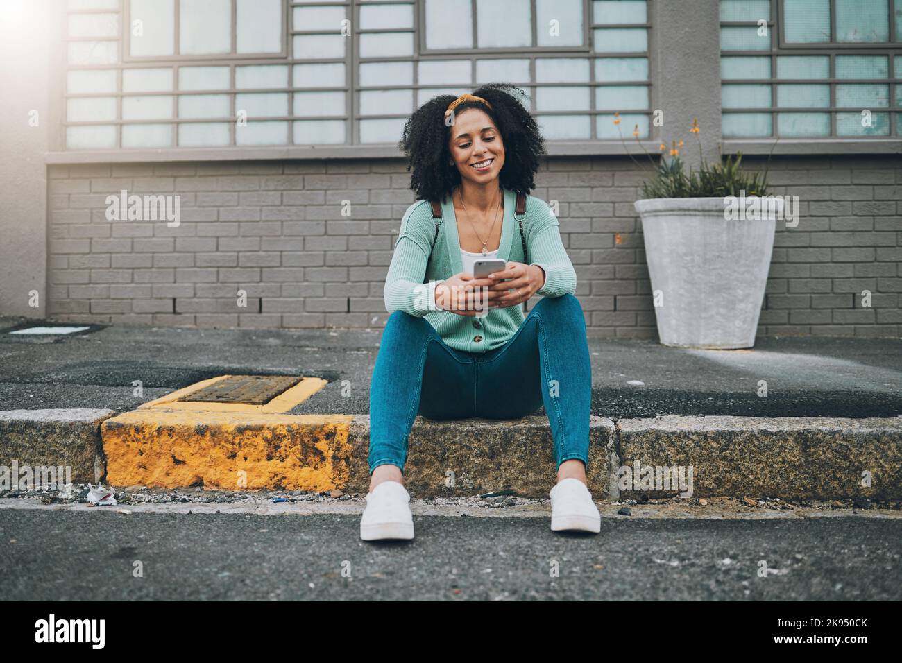 Donna nera, marciapiede della città e smartphone in mano scorrere i social media sorridere seduti sul marciapiede della strada. Donna felice, SMS al telefono e utilizzando 5g Foto Stock