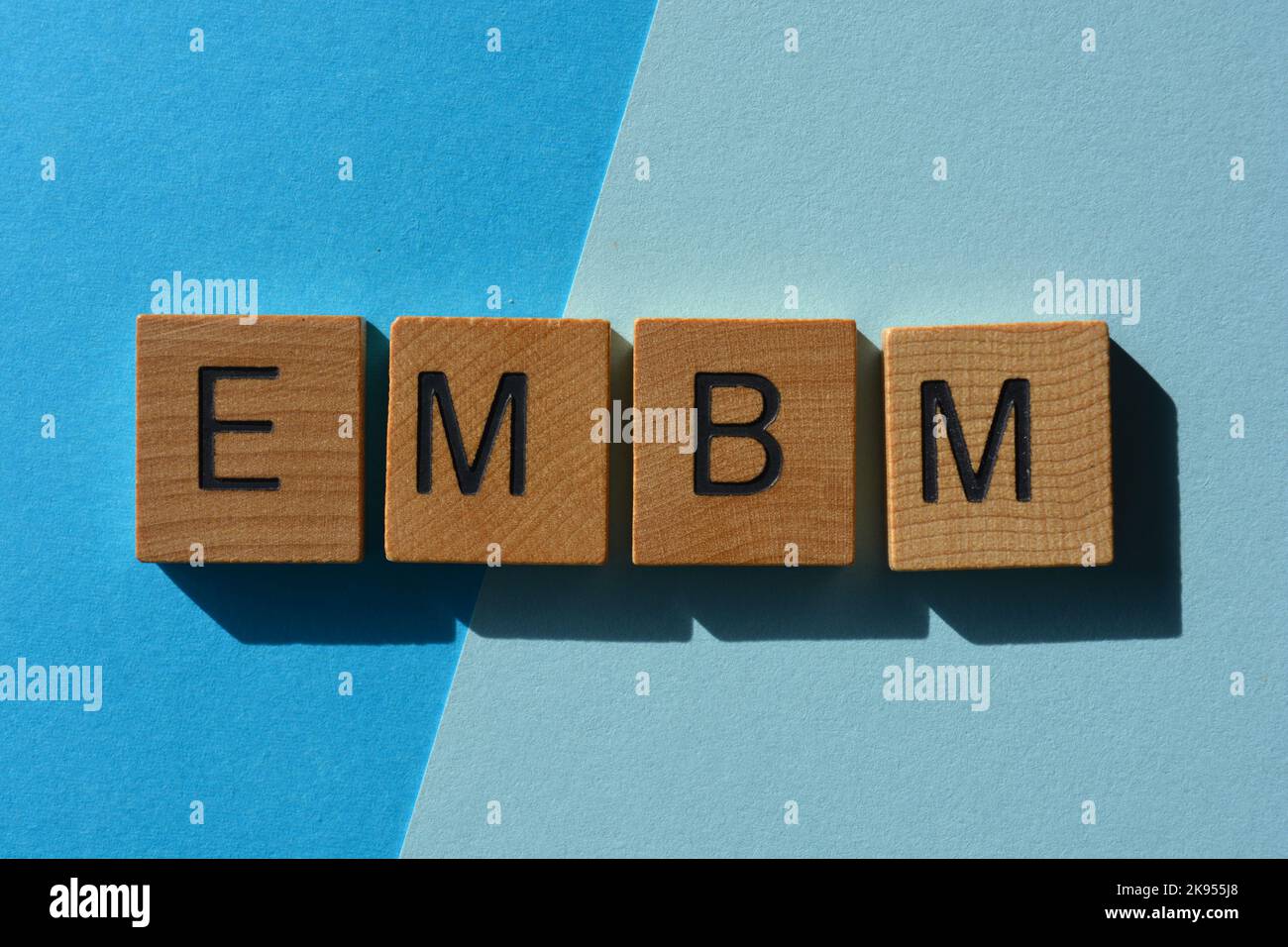 EMBM, abbreviazione di Early Morning Business Meeting, in lettere di legno isolate su sfondo blu Foto Stock