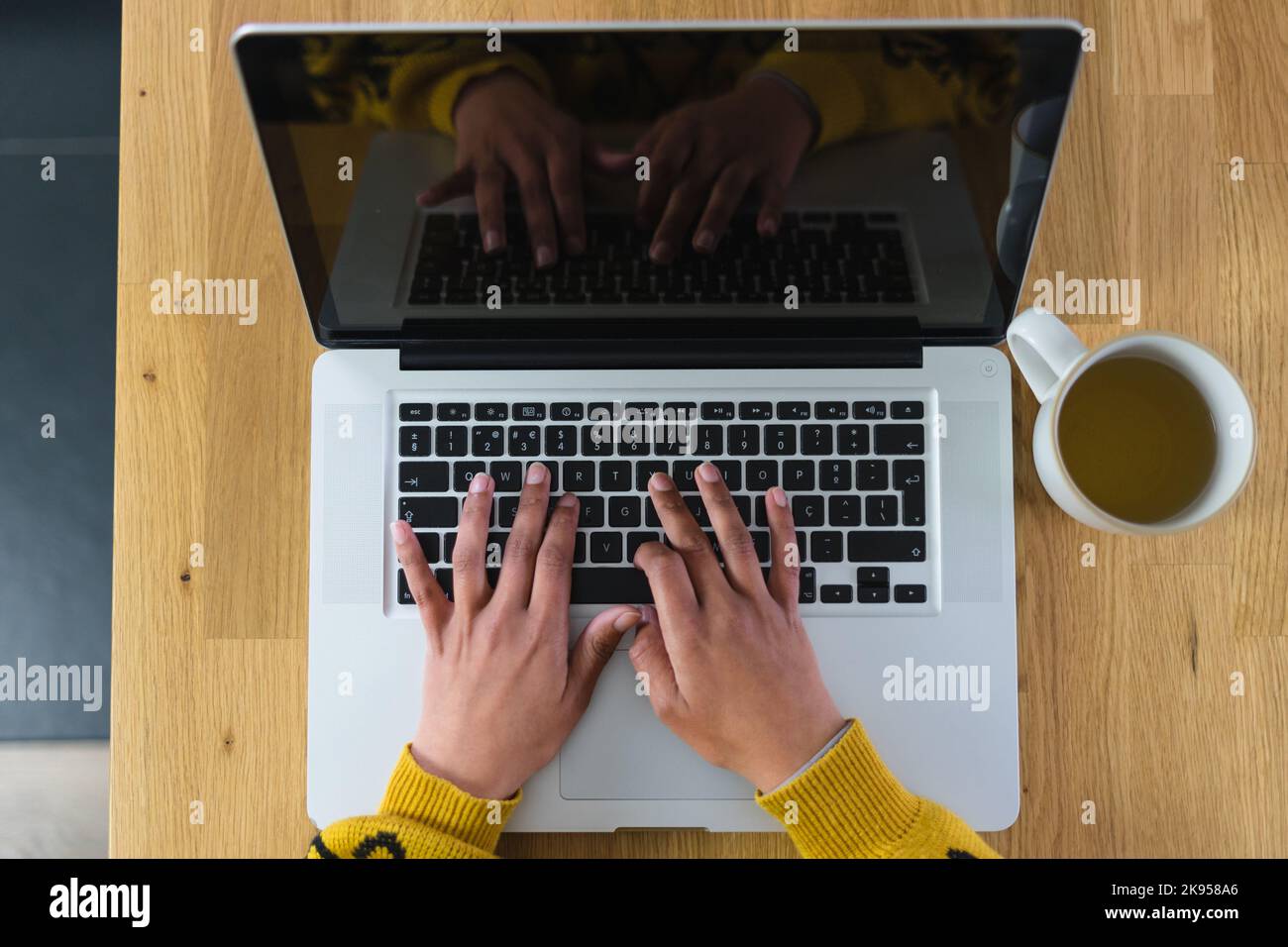 Donna che lavora sul suo computer portatile con una tazza di tè accanto a lei Foto Stock