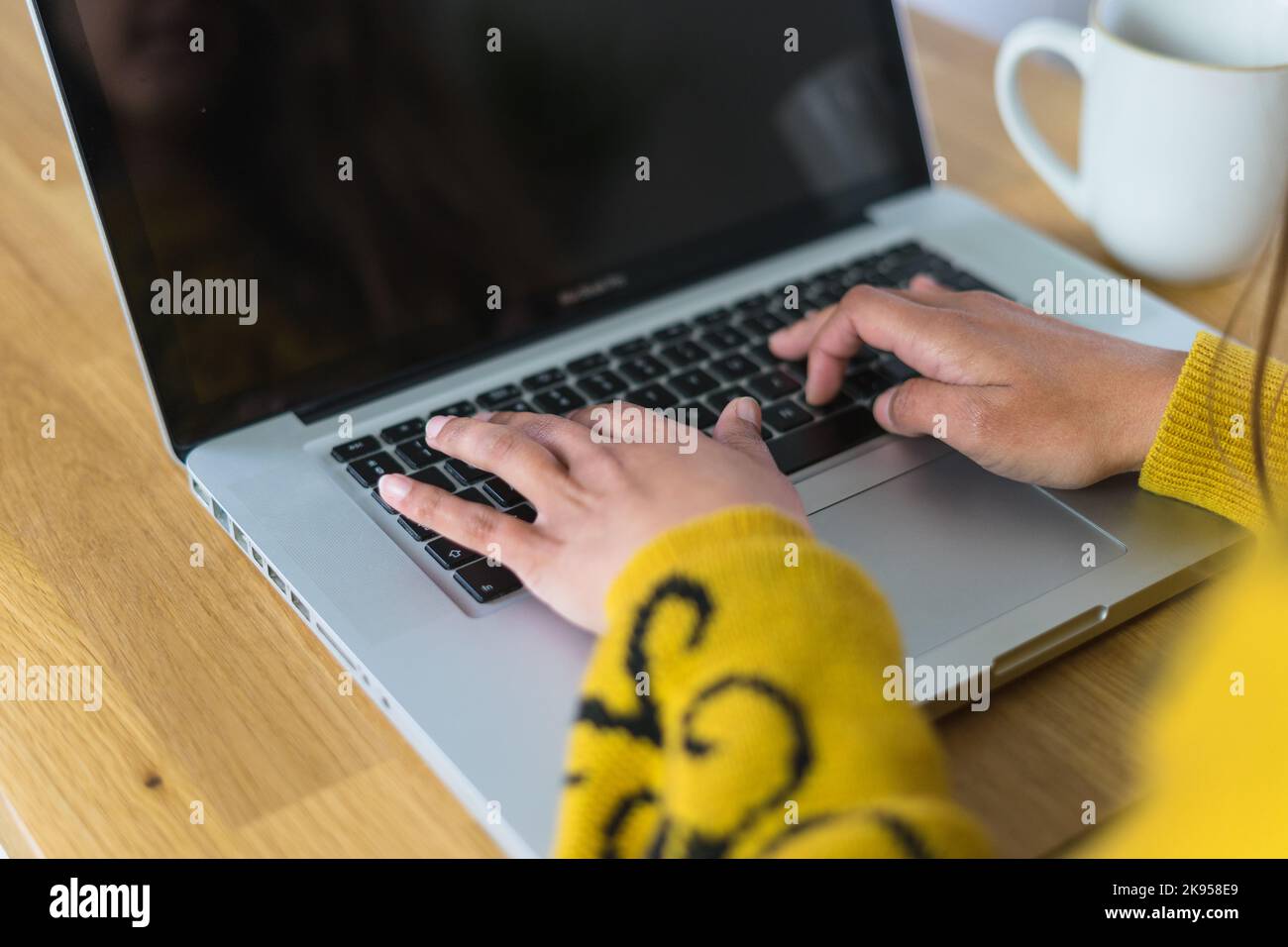 Donna che lavora sul suo computer portatile con una tazza di tè accanto a lei Foto Stock